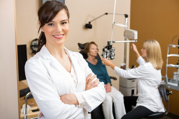 Portrait of young eye specialist with colleague examining patient in background